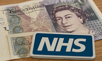 A high-resolution photograph captures a British medical professional, dressed in scrubs and a stethoscope, reviewing patient charts in a brightly lit hospital corridor. The scene highlights a calm and professional NHS healthcare environment, symbolising responsible healthcare funding and prioritisation of frontline services without text or branding.