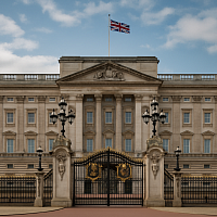 A high-resolution photograph captures Buckingham Palace under a partly cloudy sky, with the Union Jack flying prominently above its neoclassical façade. Ornate black-and-gold wrought iron gates and stone pillars frame the grand entrance, while historic lanterns and Corinthian columns highlight the palace's architectural grandeur. A symbol of British monarchy, diplomacy, and national heritage.